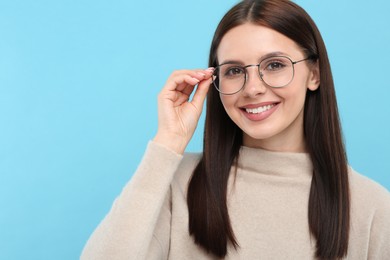 Portrait of smiling woman in stylish eyeglasses on light blue background. Space for text