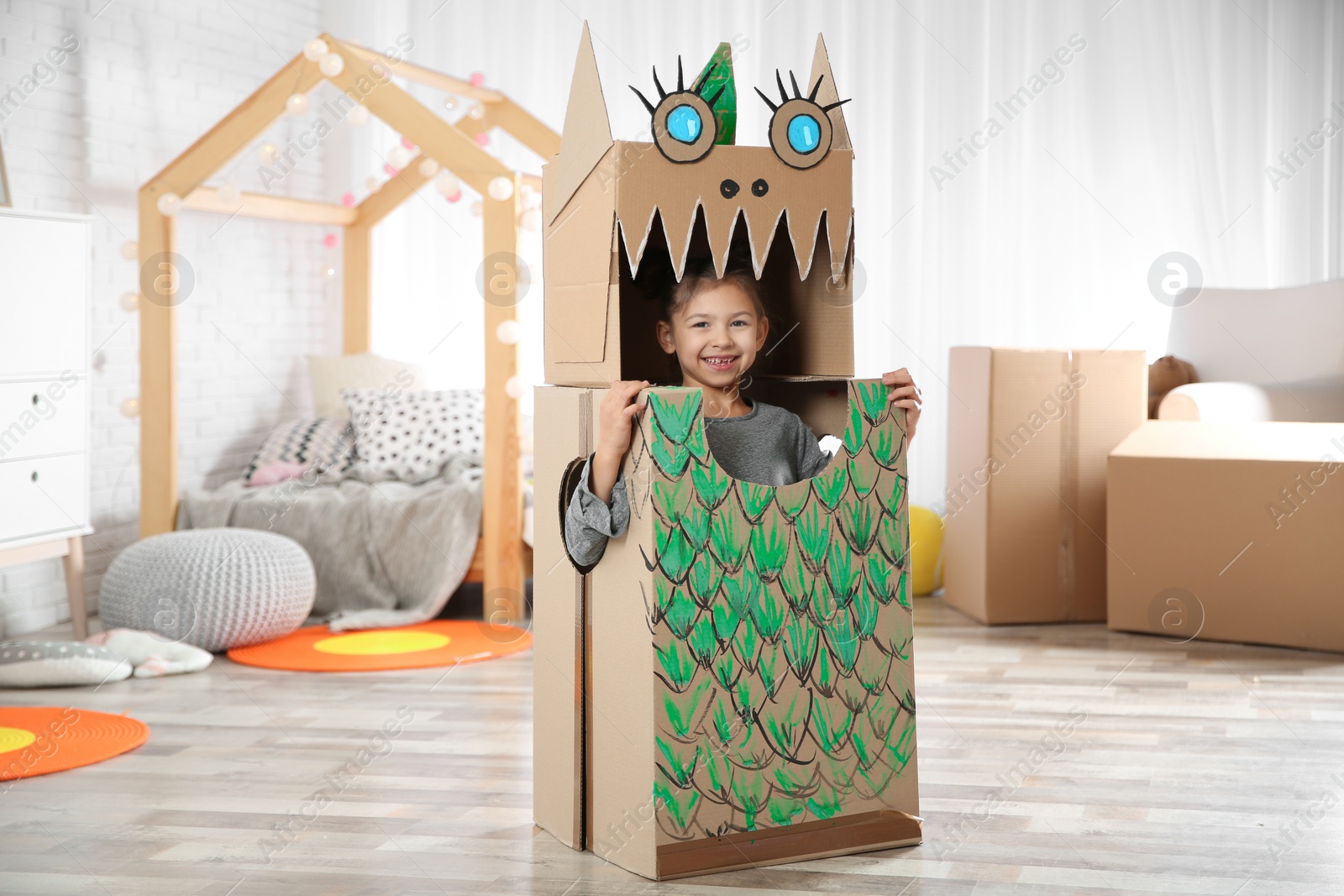 Photo of Cute little girl in cardboard costume of dinosaur at home