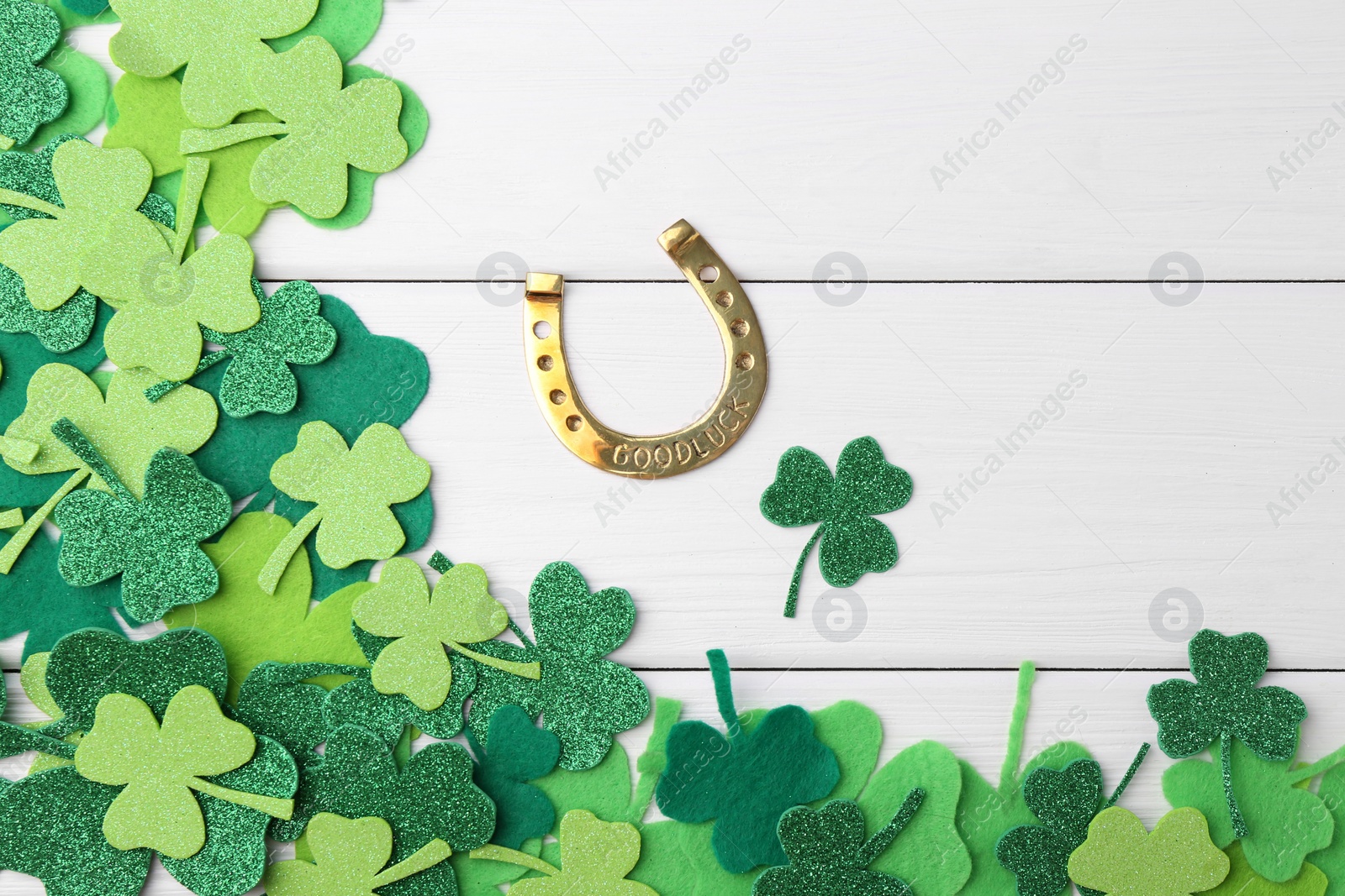 Photo of St. Patrick's day. Golden horseshoe and green decorative clover leaves on white wooden table, flat lay