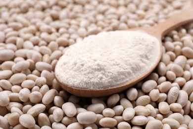 Photo of Wooden spoon with flour on white kidney beans, closeup