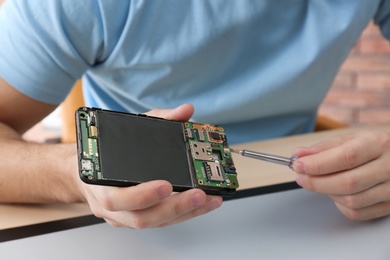 Technician repairing broken smartphone at table, closeup