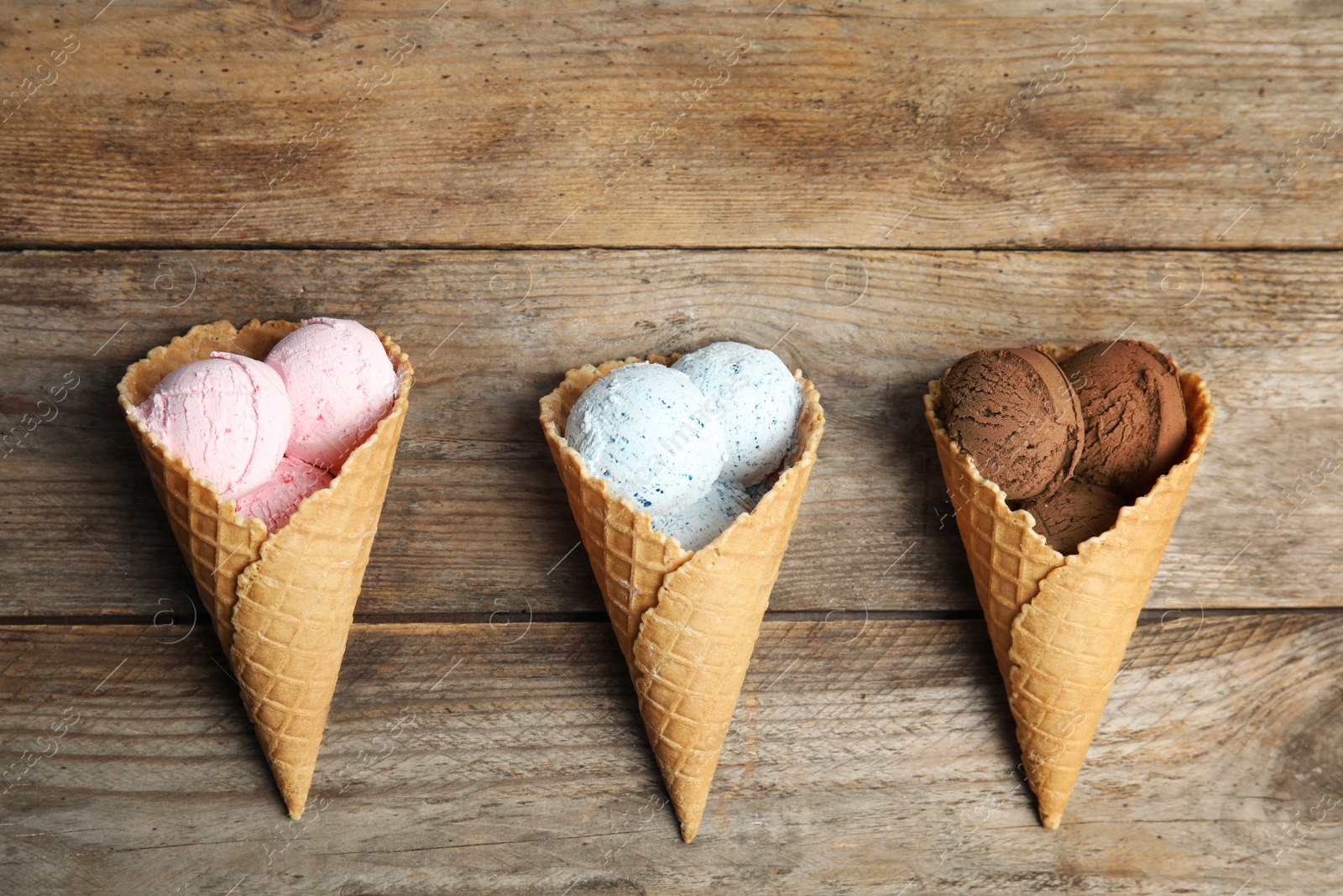 Photo of Flat lay composition with delicious ice creams in waffle cones on wooden table