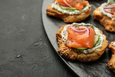 Photo of Tasty canapes with salmon, cucumber, radish and cream cheese on black table, closeup. Space for text