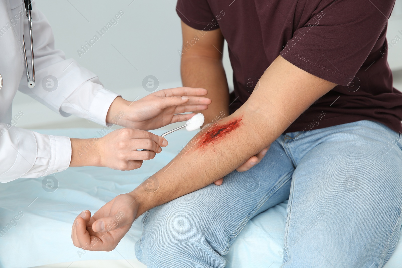 Photo of Female doctor cleaning young man's arm injury in clinic, closeup. First aid