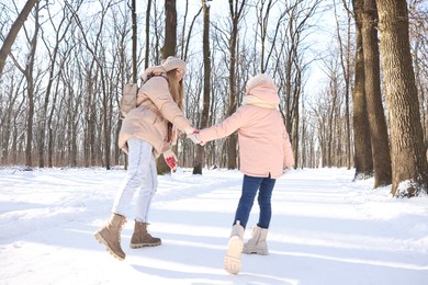 Photo of Family time. Mother and her daughter walking in sunny snowy forest, back view