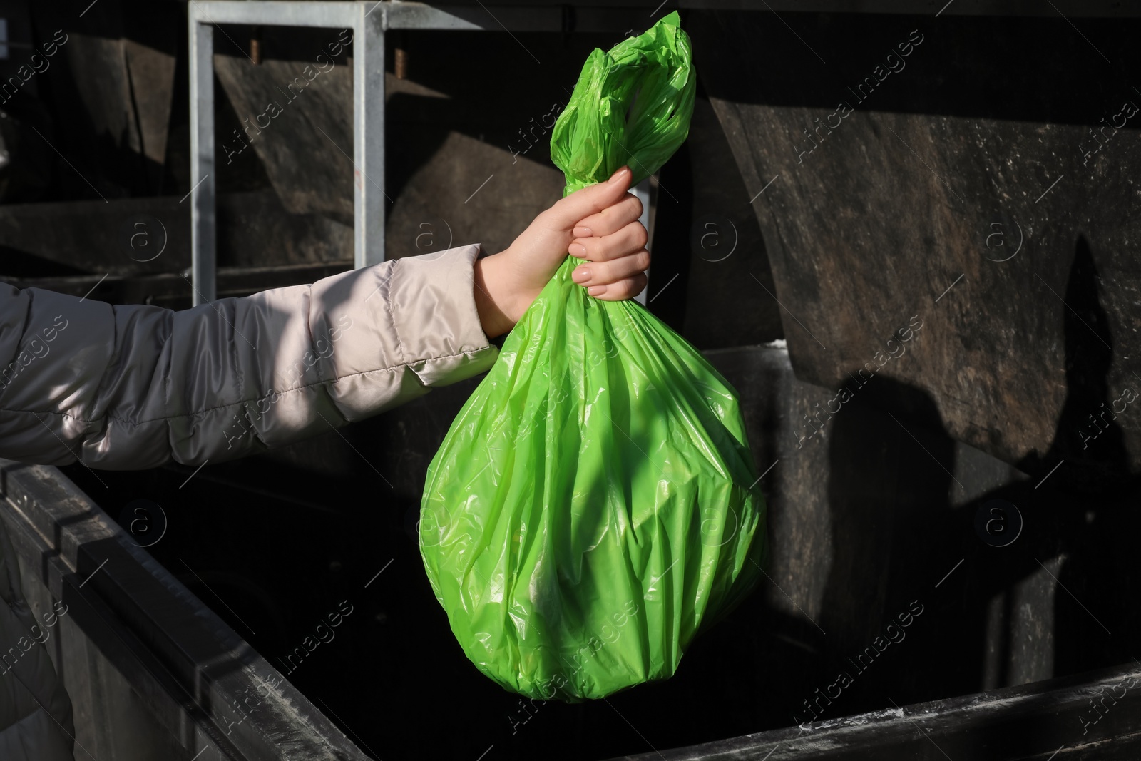 Photo of Woman throwing trash bag full of garbage in bin outdoors, closeup