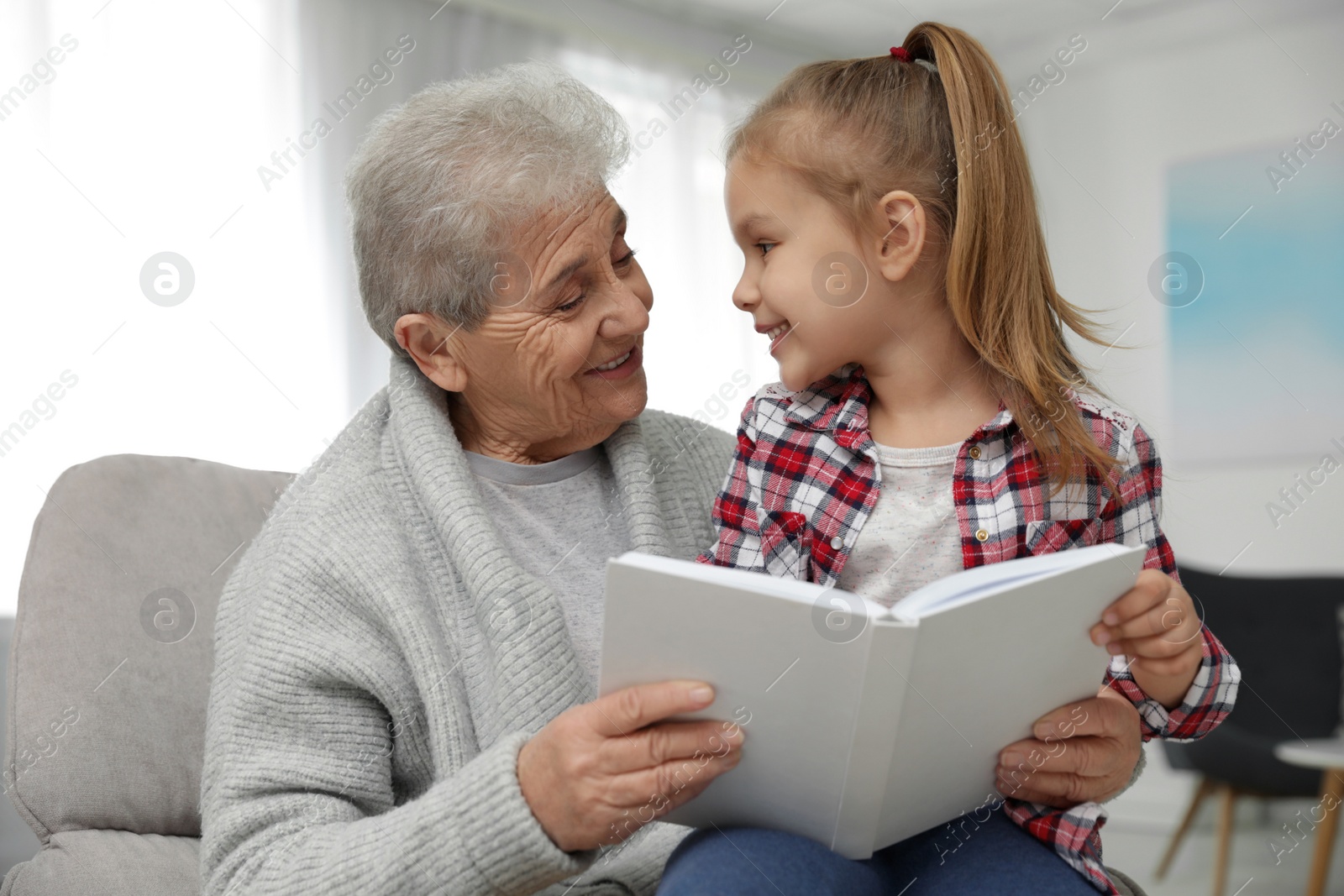 Photo of Cute girl and her grandmother reading book at home