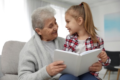 Cute girl and her grandmother reading book at home