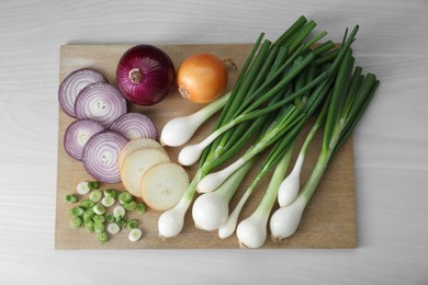 Photo of Board with different kinds of onions on white wooden table, top view