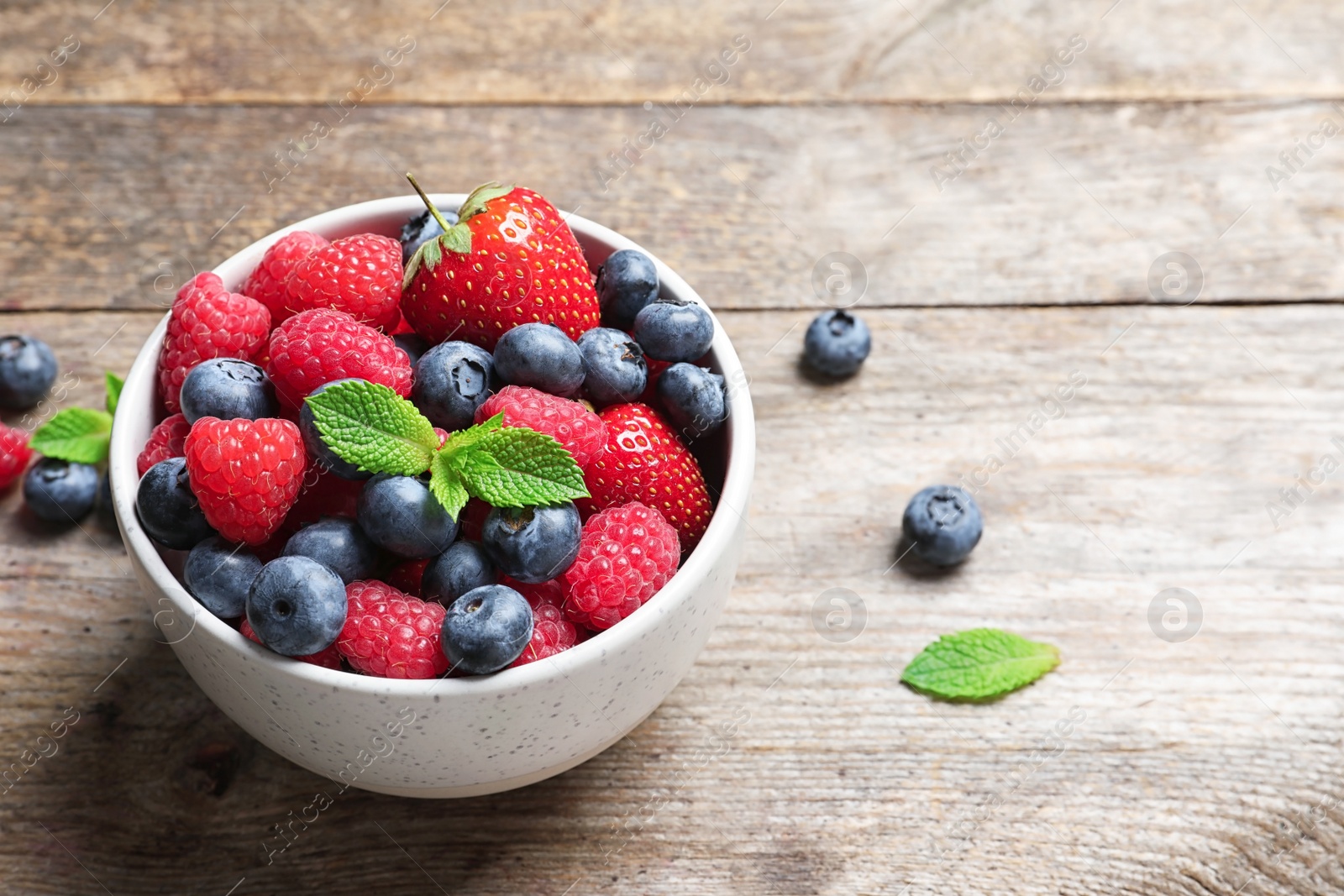 Photo of Bowl with raspberries, strawberries and blueberries on wooden table