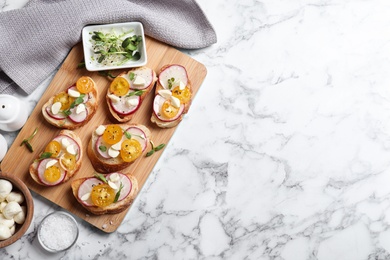 Flat lay composition of bruschettas with radish and yellow cherry tomatoes on white marble table, space for text