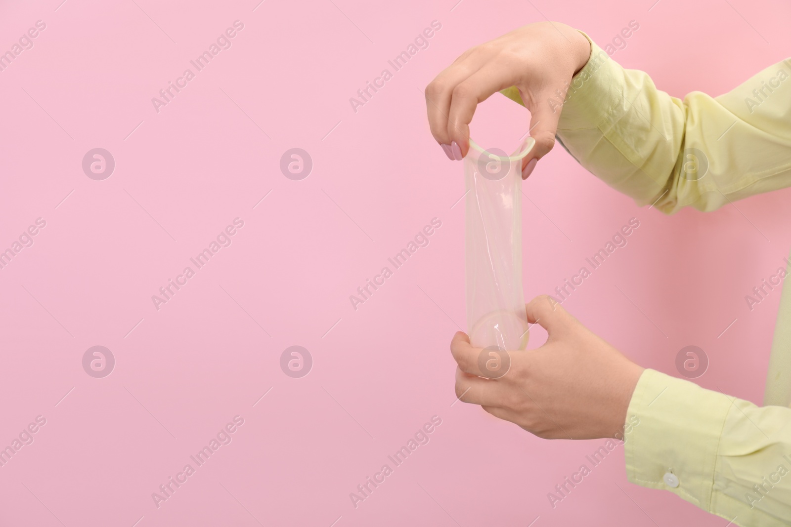 Photo of Woman with unrolled female condom on pink background, closeup. Space for text
