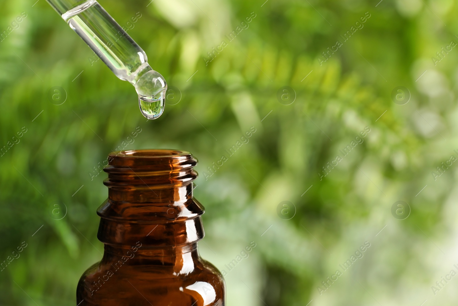 Photo of Pipette with oil over bottle on blurred background. Space for text