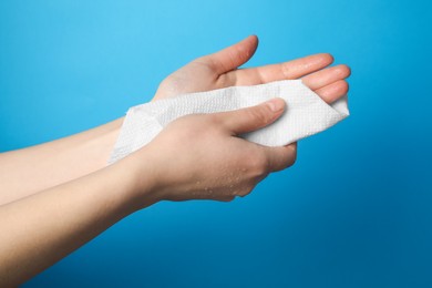 Woman wiping hands with paper towel on light blue background, closeup