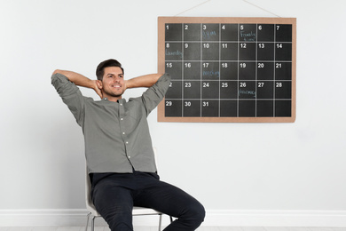 Handsome man sitting near board calendar indoors