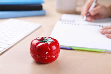 Woman writing in notebook at wooden table, focus on kitchen timer in shape of tomato. Space for text
