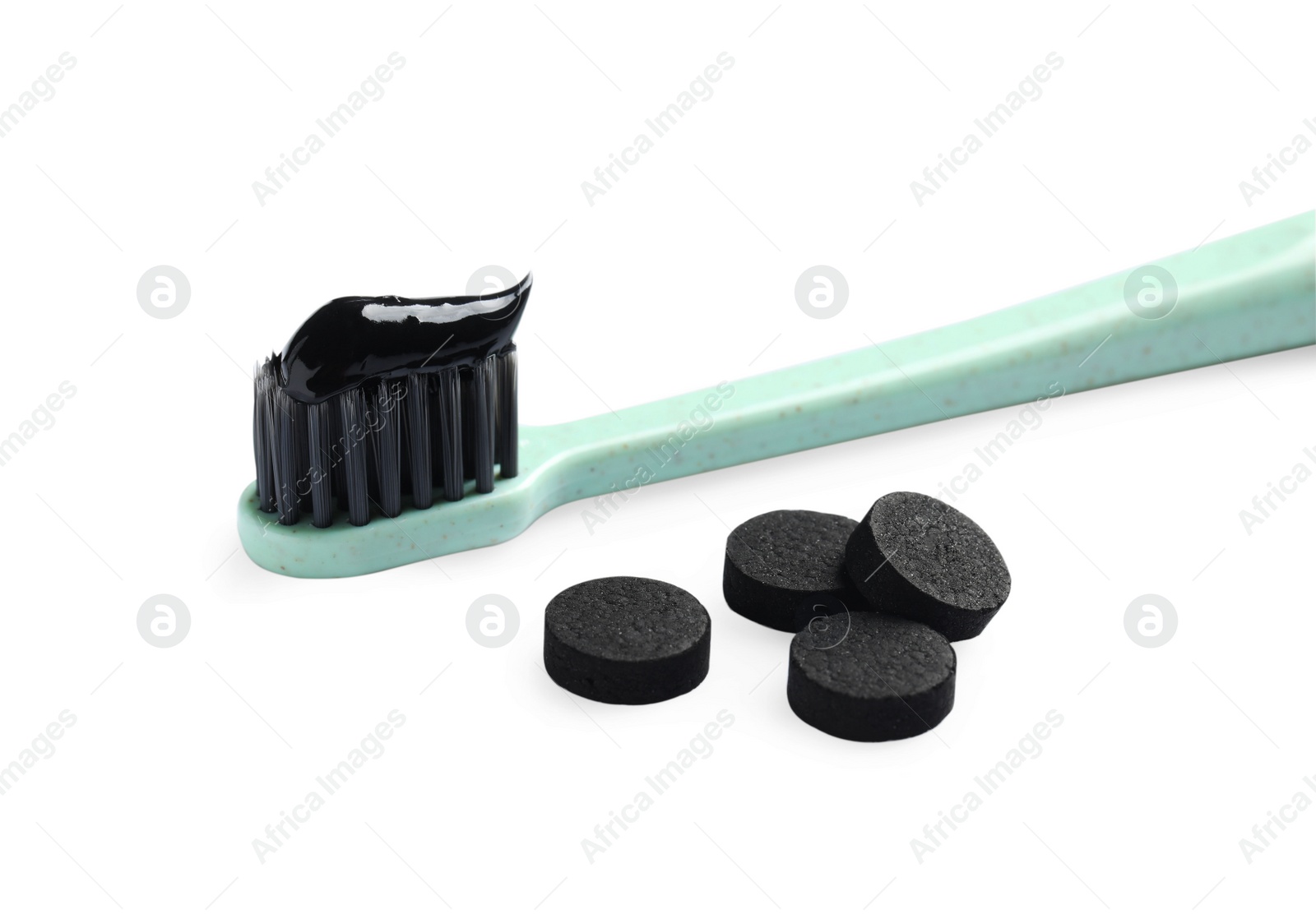 Photo of Brush with charcoal toothpaste and black pills on white background