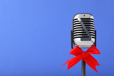 Photo of Retro microphone with red bow on blue background, space for text. Christmas music