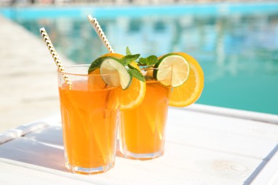 Photo of Refreshing cocktail in glasses near outdoor swimming pool on sunny day