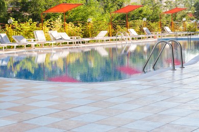 Outdoor swimming pool and many empty loungers at resort on sunny day