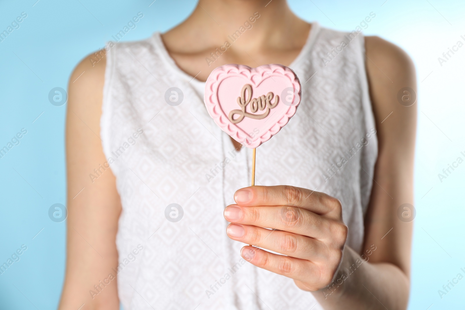 Photo of Woman holding heart shaped lollipop made of chocolate on light blue background, closeup