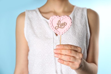 Woman holding heart shaped lollipop made of chocolate on light blue background, closeup