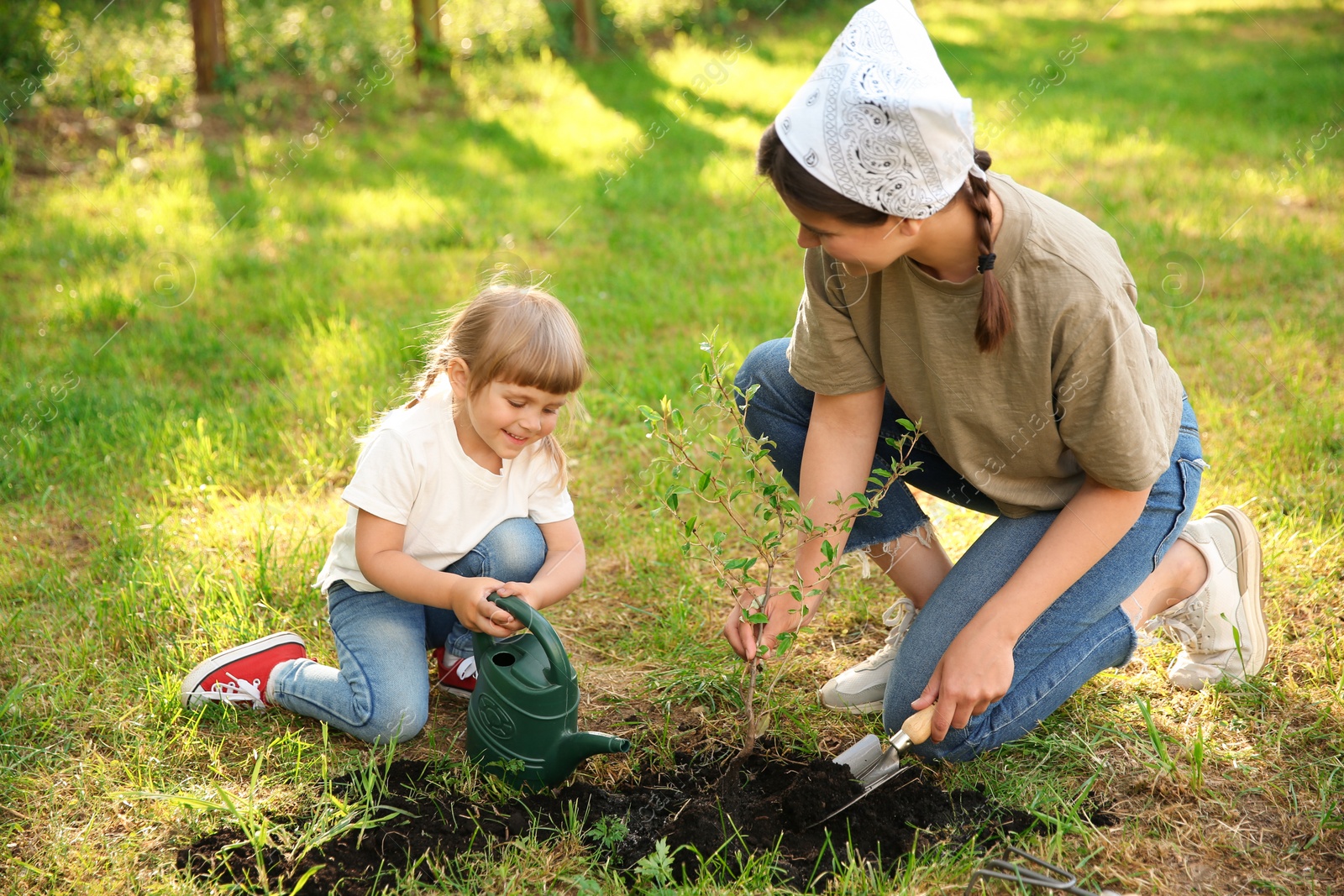 Photo of Mother and her daughter planting tree together in garden