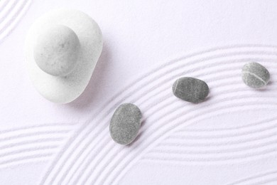 Photo of Zen garden stones on white sand with pattern, flat lay