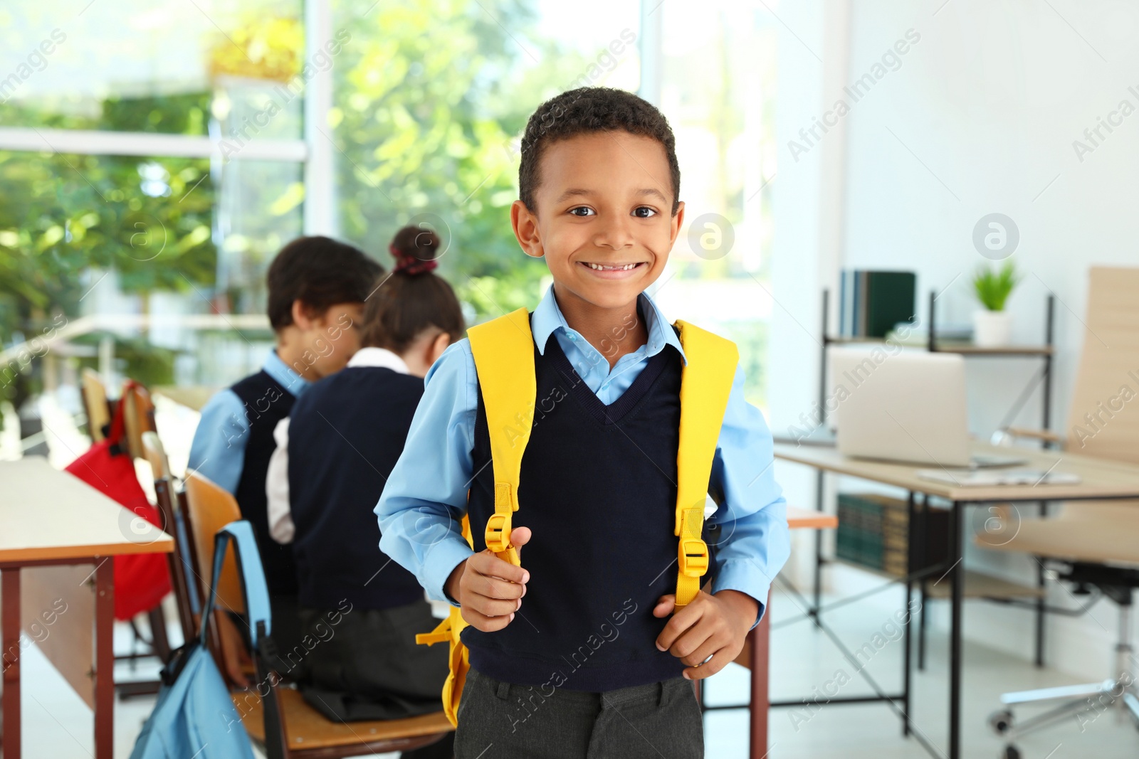 Photo of African-American boy wearing school uniform with backpack in classroom