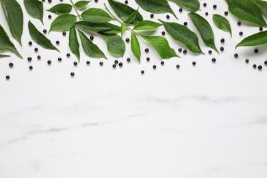Photo of Ripe elderberries with green leaves on white marble table, flat lay. Space for text