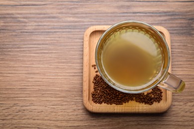 Photo of Cup of aromatic buckwheat tea and granules on wooden table, top view. Space for text