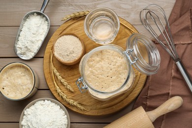 Photo of Leaven, ears of wheat, whisk, rolling pin, water and flour on beige wooden table, flat lay