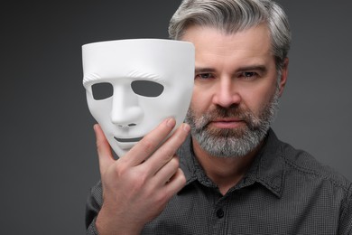 Multiple personality concept. Man with mask on dark grey background
