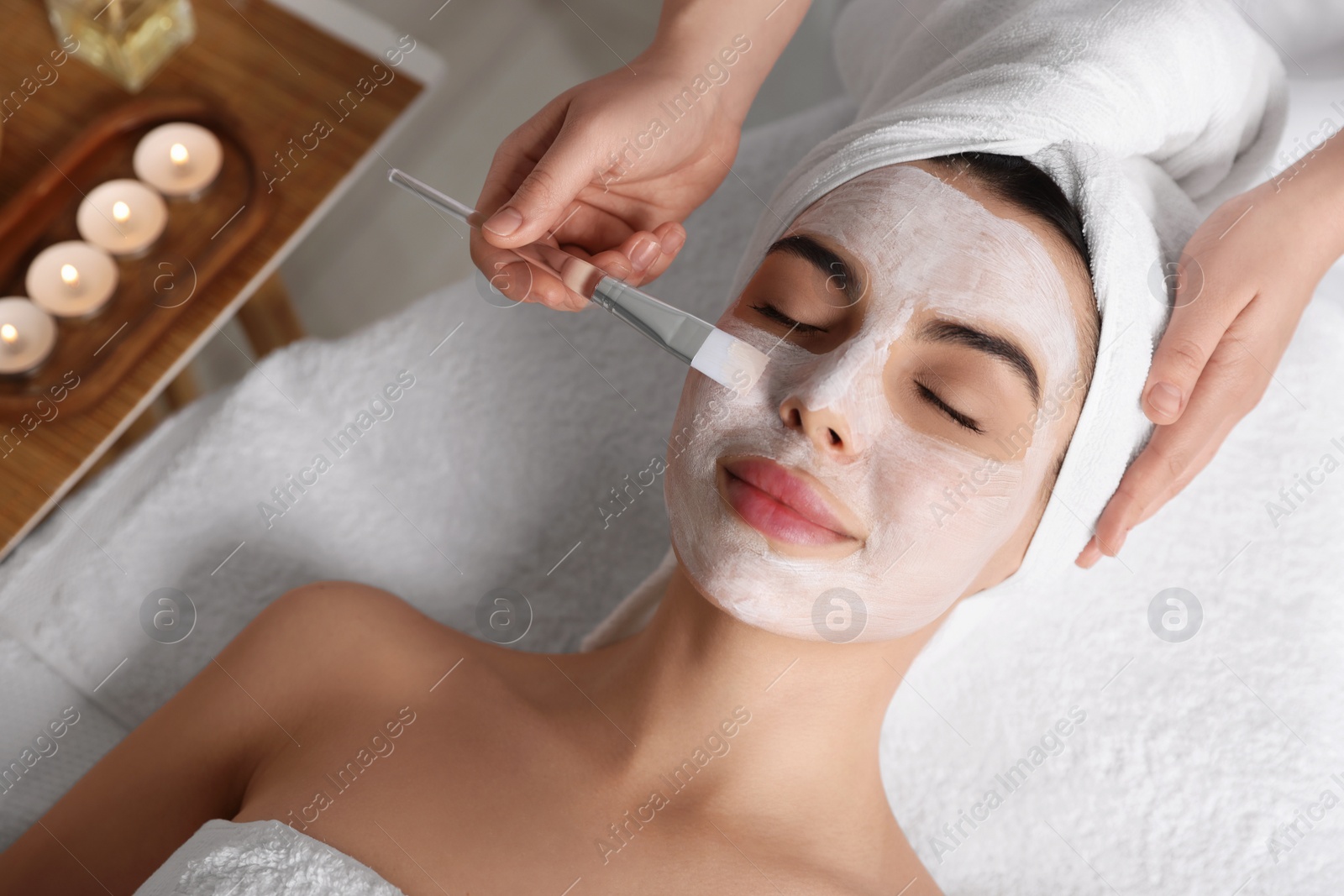 Photo of Cosmetologist applying mask on woman's face in spa salon, above view