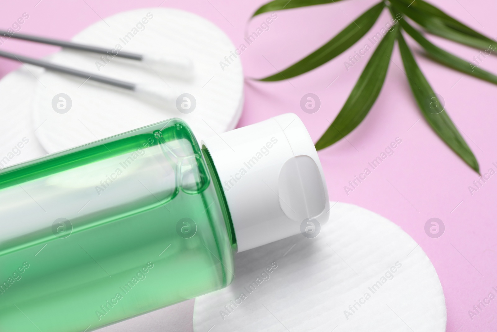 Photo of Bottle of micellar water, twig, cotton pads and swabs on pink background, closeup