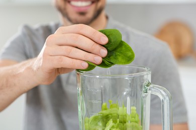 Photo of Man adding spinach leaves into blender with ingredients for smoothie in kitchen, closeup