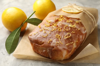 Photo of Wrapped tasty lemon cake with glaze and citrus fruits on light grey textured table, closeup