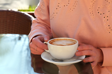 Woman with cup of fresh aromatic coffee at table in cafe