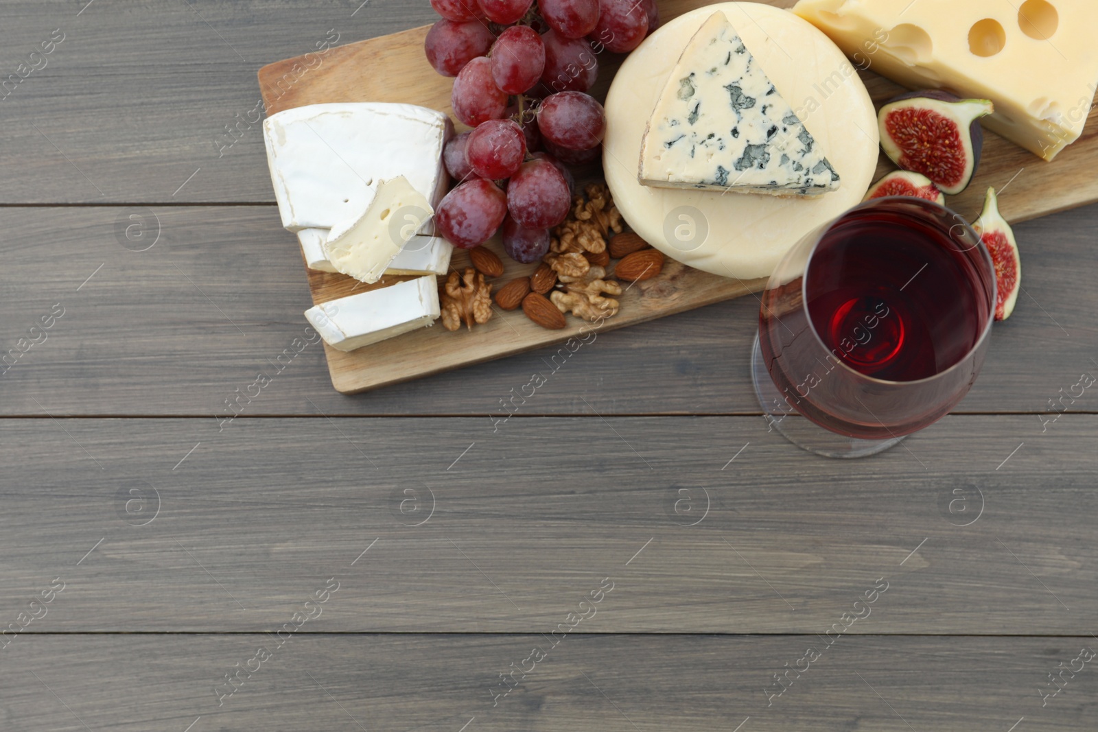 Photo of Different types of delicious cheeses, snacks and wine on wooden table, top view. Space for text