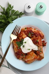 Delicious stuffed cabbage rolls served with sour cream on white table, flat lay