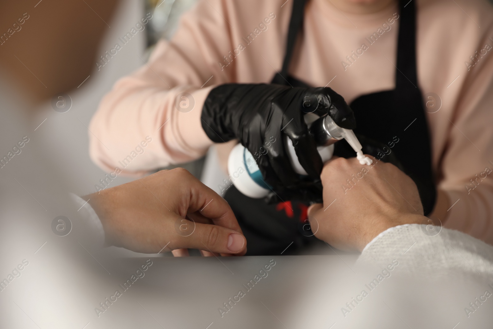 Photo of Professional manicurist applying cream on client's hand in beauty salon, closeup