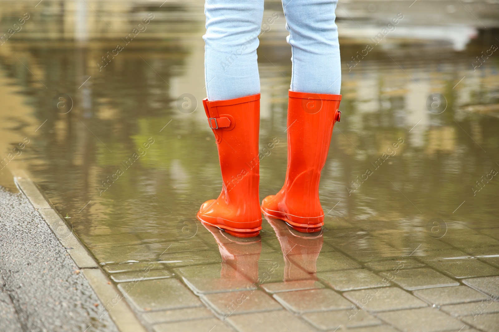 Photo of Woman with red rubber boots in puddle, closeup. Rainy weather