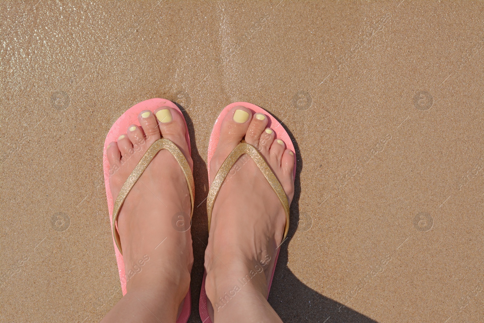 Photo of Woman in stylish pink flip flops standing on wet sand, top view. Space for text