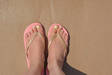 Woman in stylish pink flip flops standing on wet sand, top view. Space for text