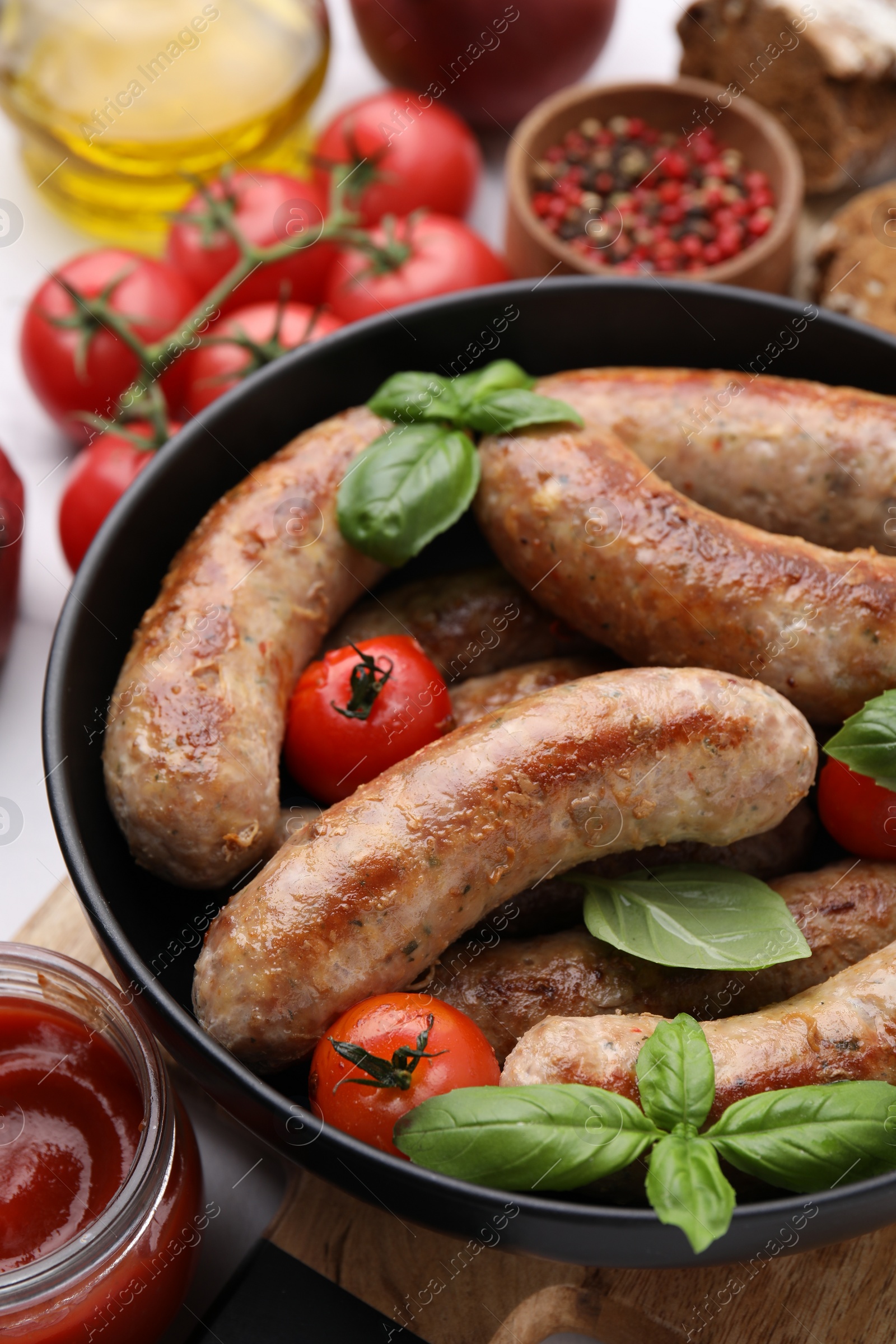 Photo of Bowl with tasty homemade sausages, basil leaves and tomatoes on table, closeup