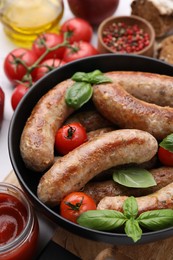 Photo of Bowl with tasty homemade sausages, basil leaves and tomatoes on table, closeup