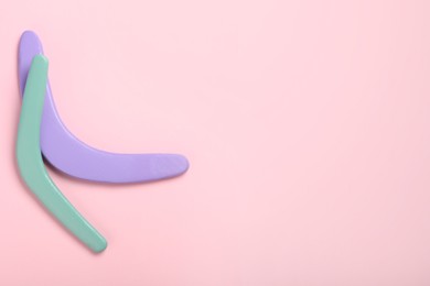Colorful wooden boomerangs on pink background, flat lay. Space for text