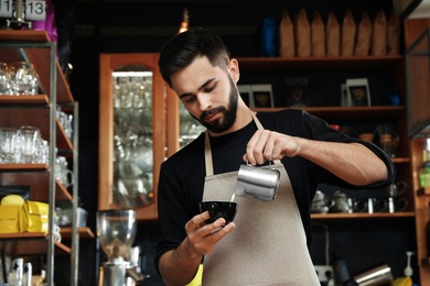 Photo of Portraitbarista pouring milk into cup of coffee against bar shelves in cafe