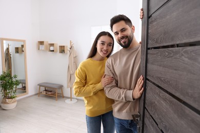 Photo of Happy couple standing near door, space for text. Invitation to come indoors