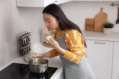 Photo of Beautiful woman cooking and smelling soup in kitchen
